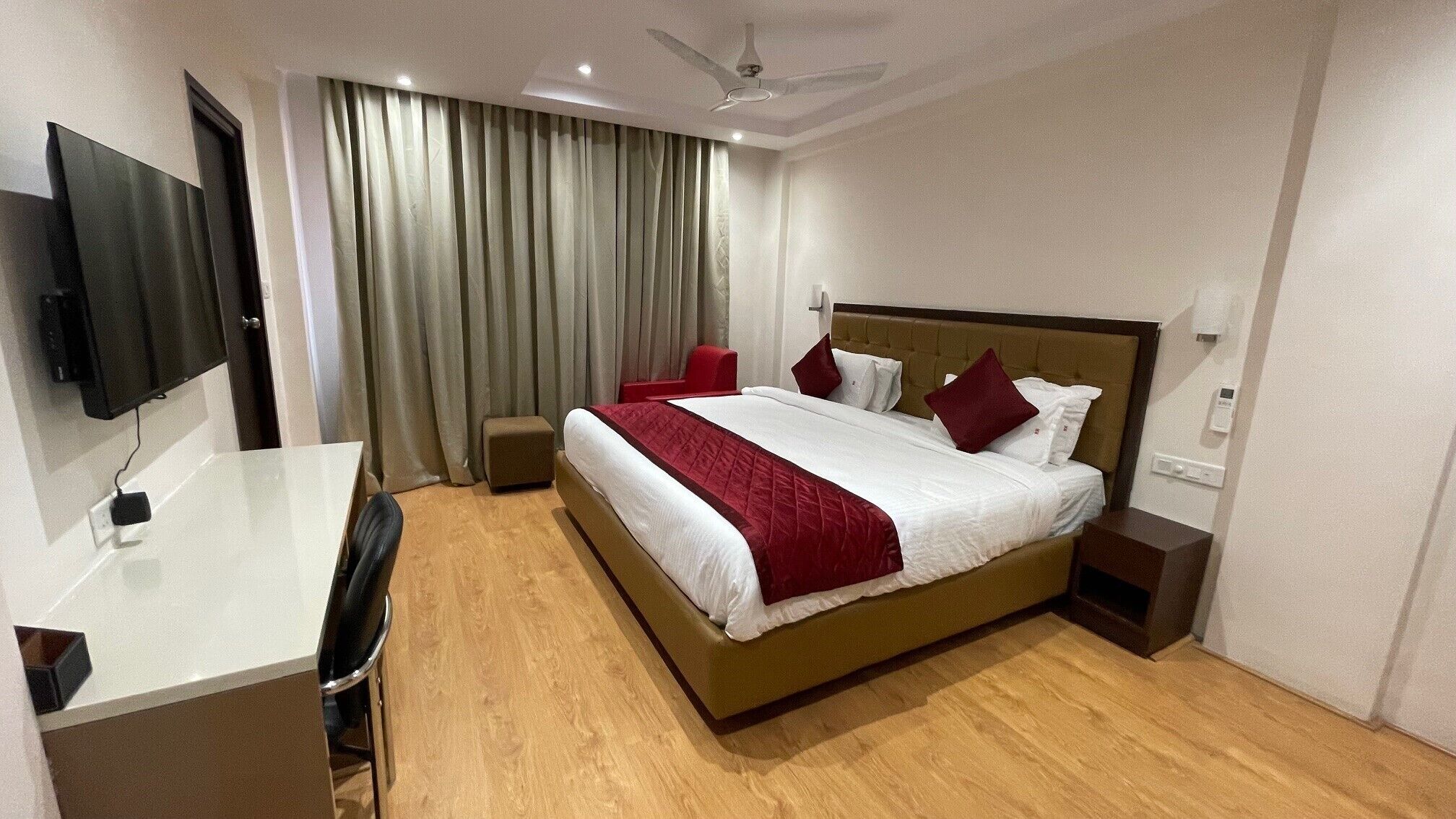 A hotel room with a large bed, a desk, a chair, a TV, and a ceiling fan.