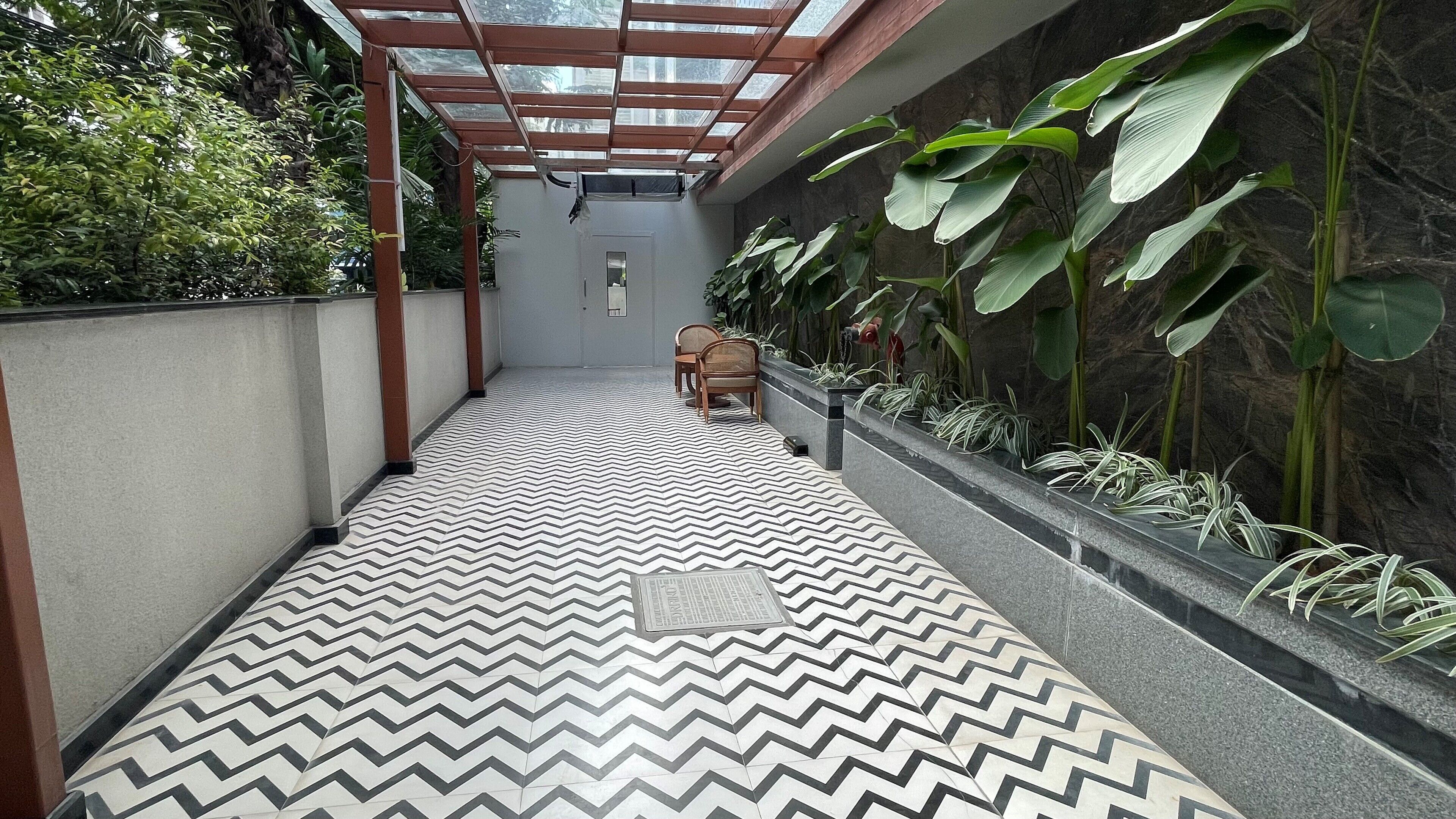 A corridor with a zigzag patterned floor, a glass ceiling, and a seating area with chairs.