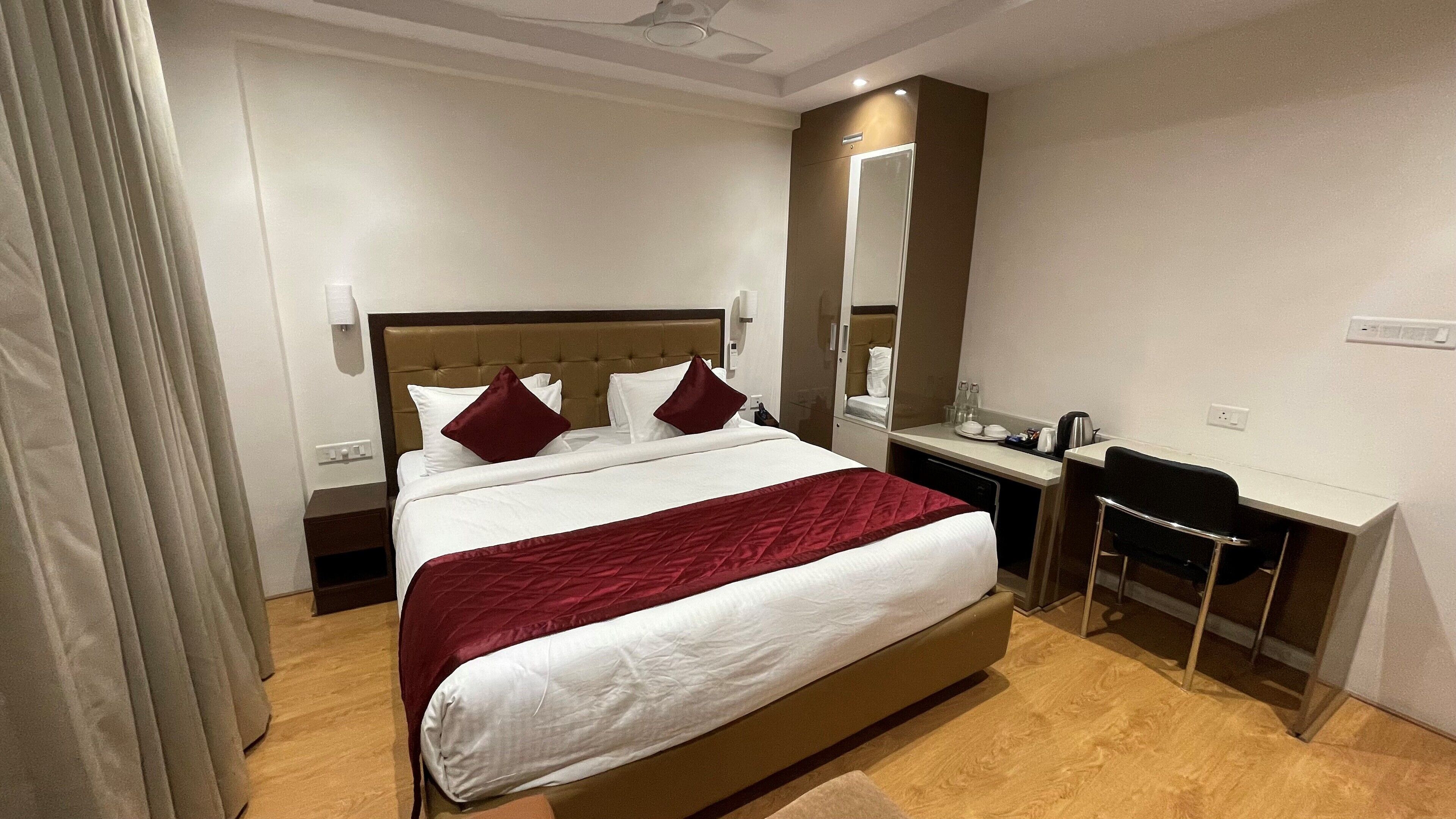 A hotel room with a bed, bedside table, desk, chair, and a mirror.