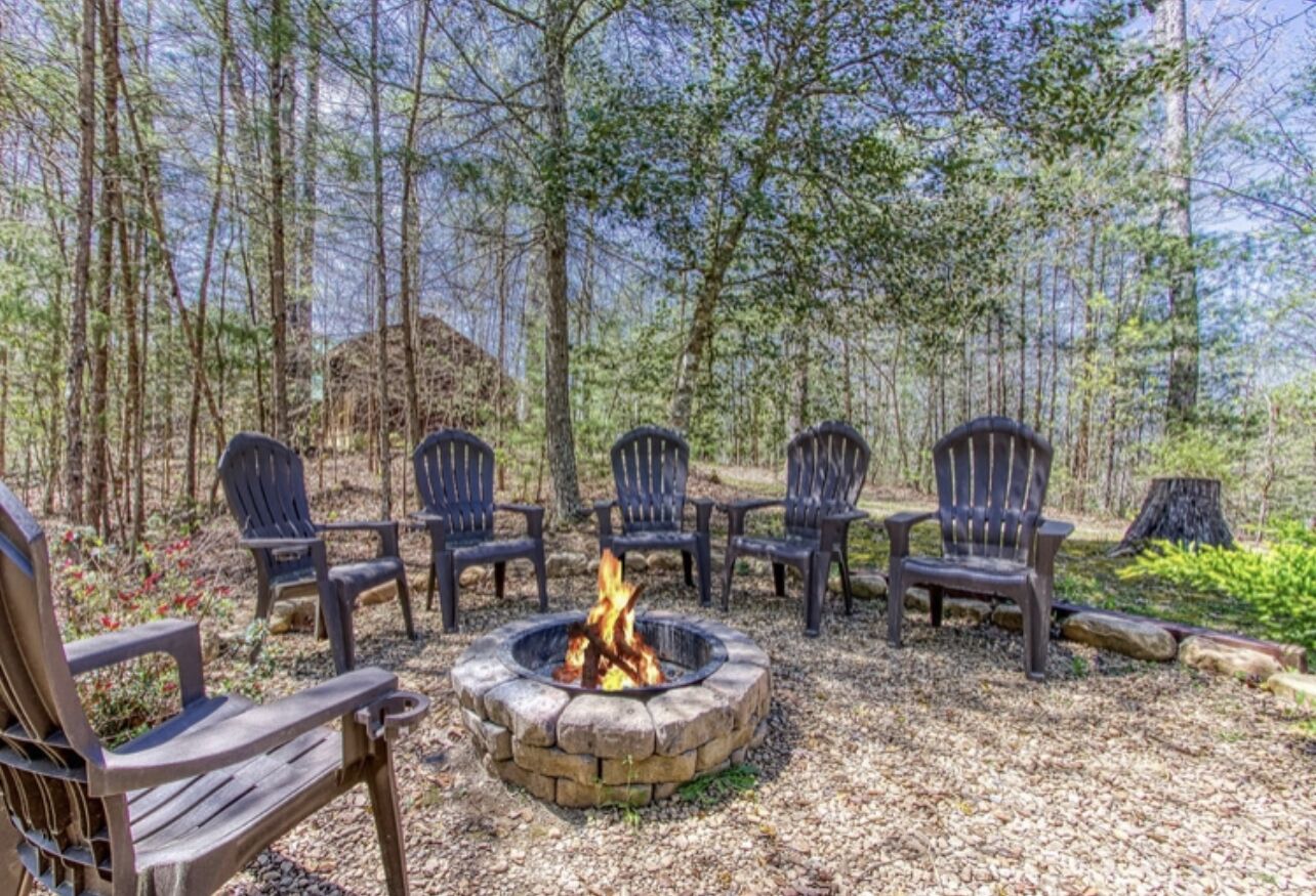 Un foyer entouré de fauteuils Adirondack, le tout situé dans un cadre forestier.