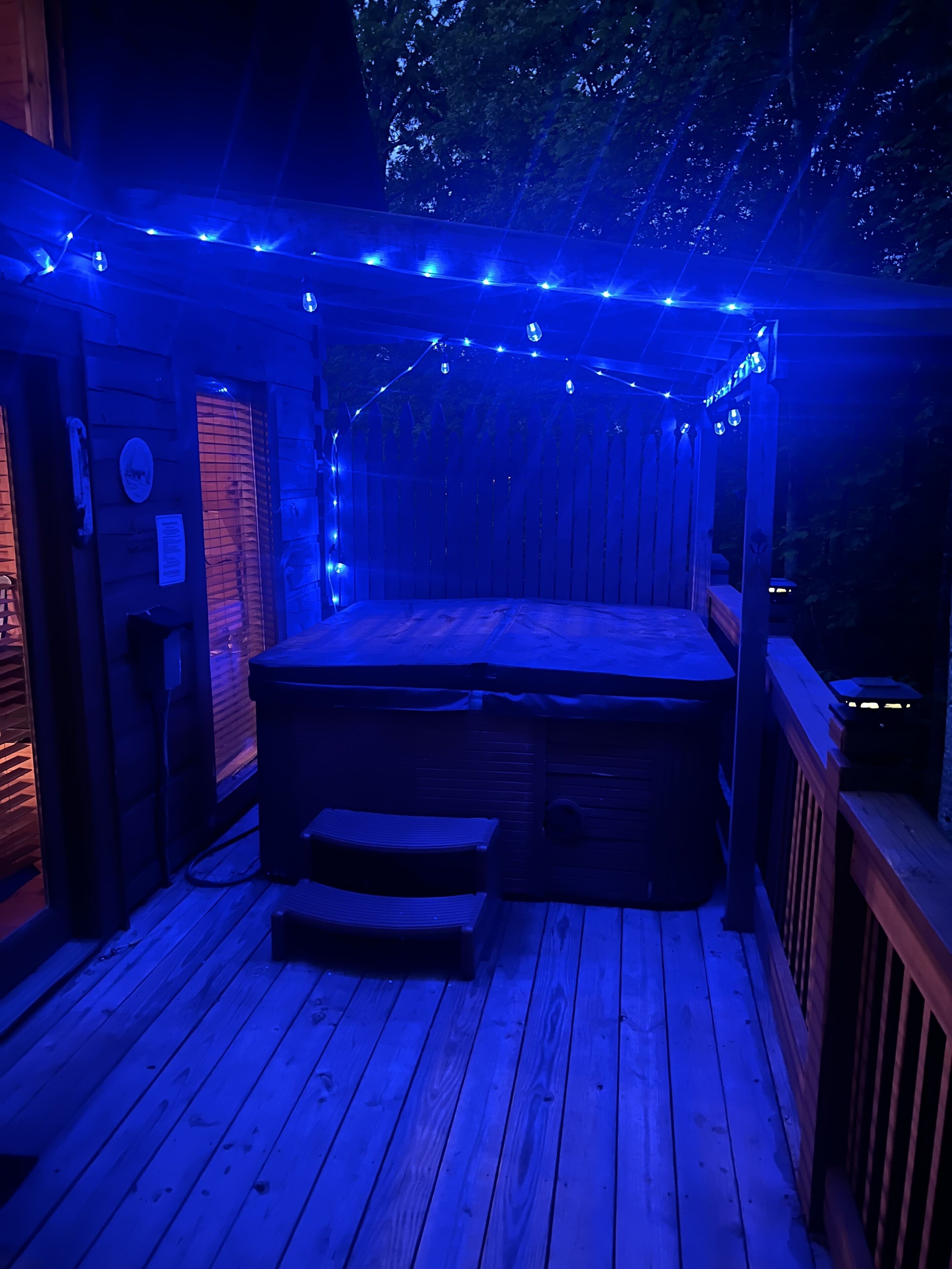 Une terrasse en bois avec un jacuzzi, des guirlandes lumineuses et une rambarde en bois.