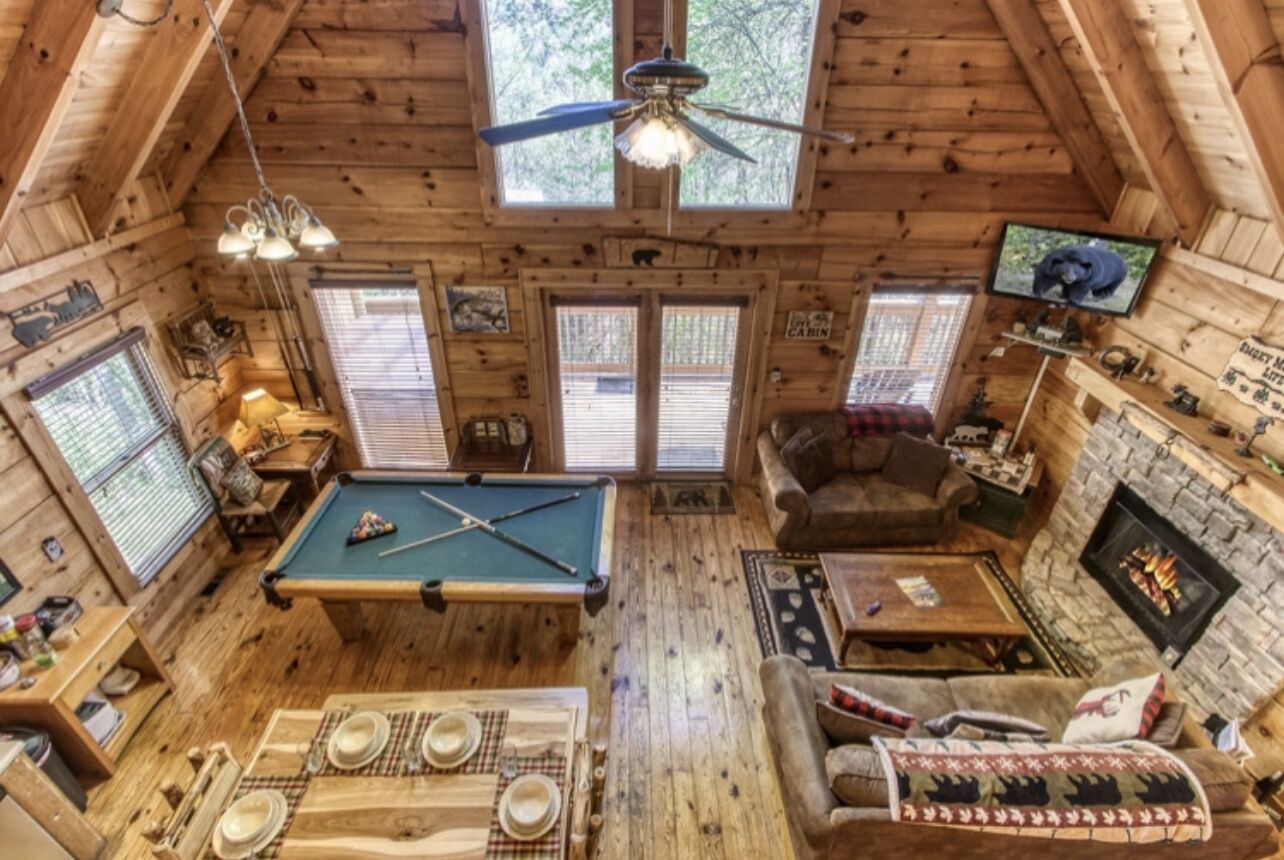 A cozy cabin interior with a pool table, a fireplace, and a television.