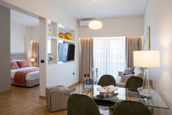 Quarto de hotel com cama, televisão, mesa de vidro, sofá e luminária.