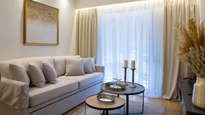 Una sala de estar con sofá, mesa de centro, un cuadro y una ventana con cortinas.
