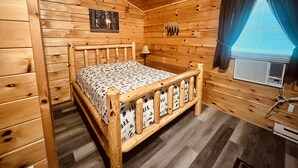 A wooden cabin room with a bed, a picture on the wall, and a window with curtains. - Log Cabin with Hot Tub 2 Miles from Crystal Mountain!!! (Thompsonville)