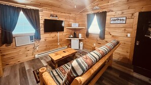 A cozy cabin with a wooden interior, a sofa, a TV, a small table, and a microwave. - Log Cabin with Hot Tub 2 Miles from Crystal Mountain!!! (Thompsonville)