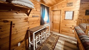 A cozy cabin interior with wooden walls, a bench, a small table, and a door marked "The Cabin is My Happy Place". - Log Cabin with Hot Tub 2 Miles from Crystal Mountain!!! (Thompsonville)