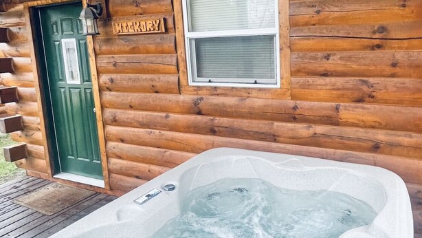 A hot tub in front of a wooden cabin with a green door and a window above it. - Log Cabin with Hot Tub 2 Miles from Crystal Mountain!!! (Thompsonville)