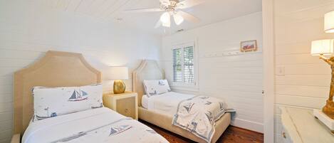 A bedroom with two beds, a ceiling fan, a window with blinds, and a dresser.
