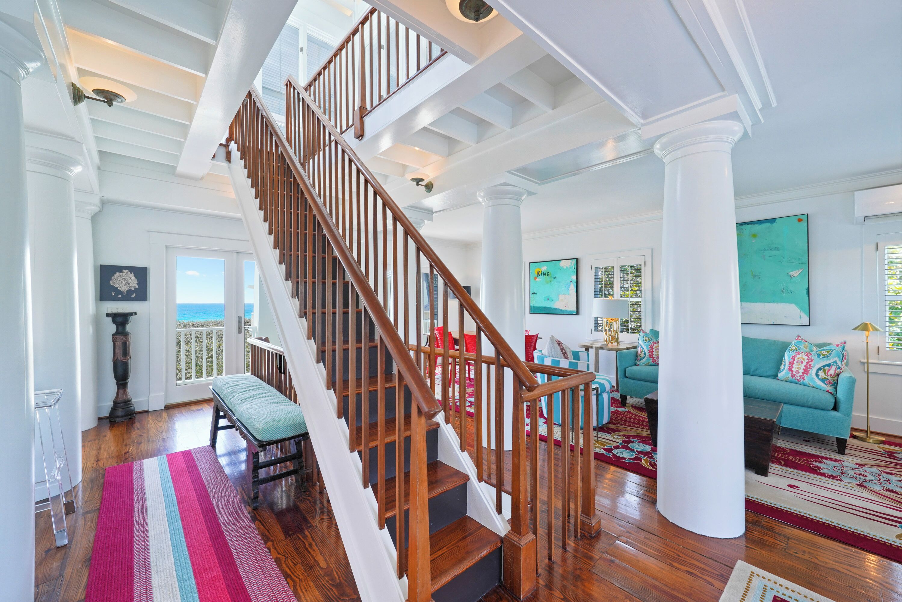 Un interior espacioso con una escalera de madera, vistas al exterior y un sofá color turquesa.