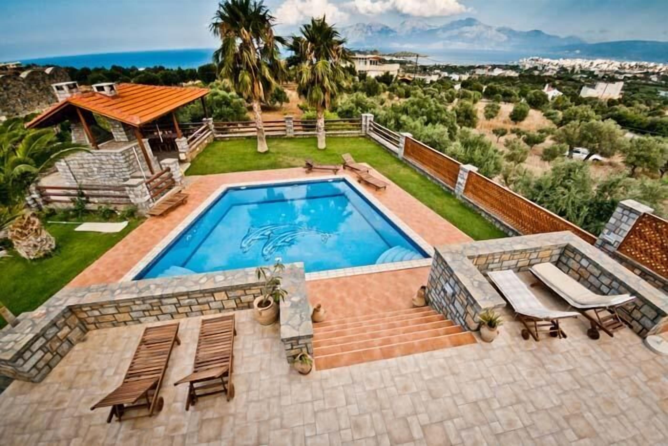 Una piscina con terraza de piedra, sillas de descanso y vista al mar.