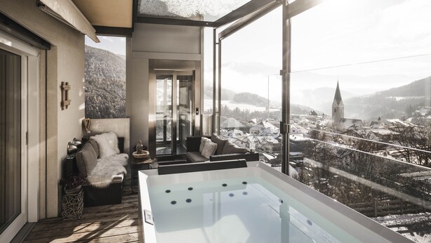 A modern interior with a glass-enclosed jacuzzi, a cozy seating area, and a panoramic view of a snowy town. - Dolomites Alpin Penthouse 90 qm with privat sauna and privat whirlpool, WLAN (Rio di Pusteria)