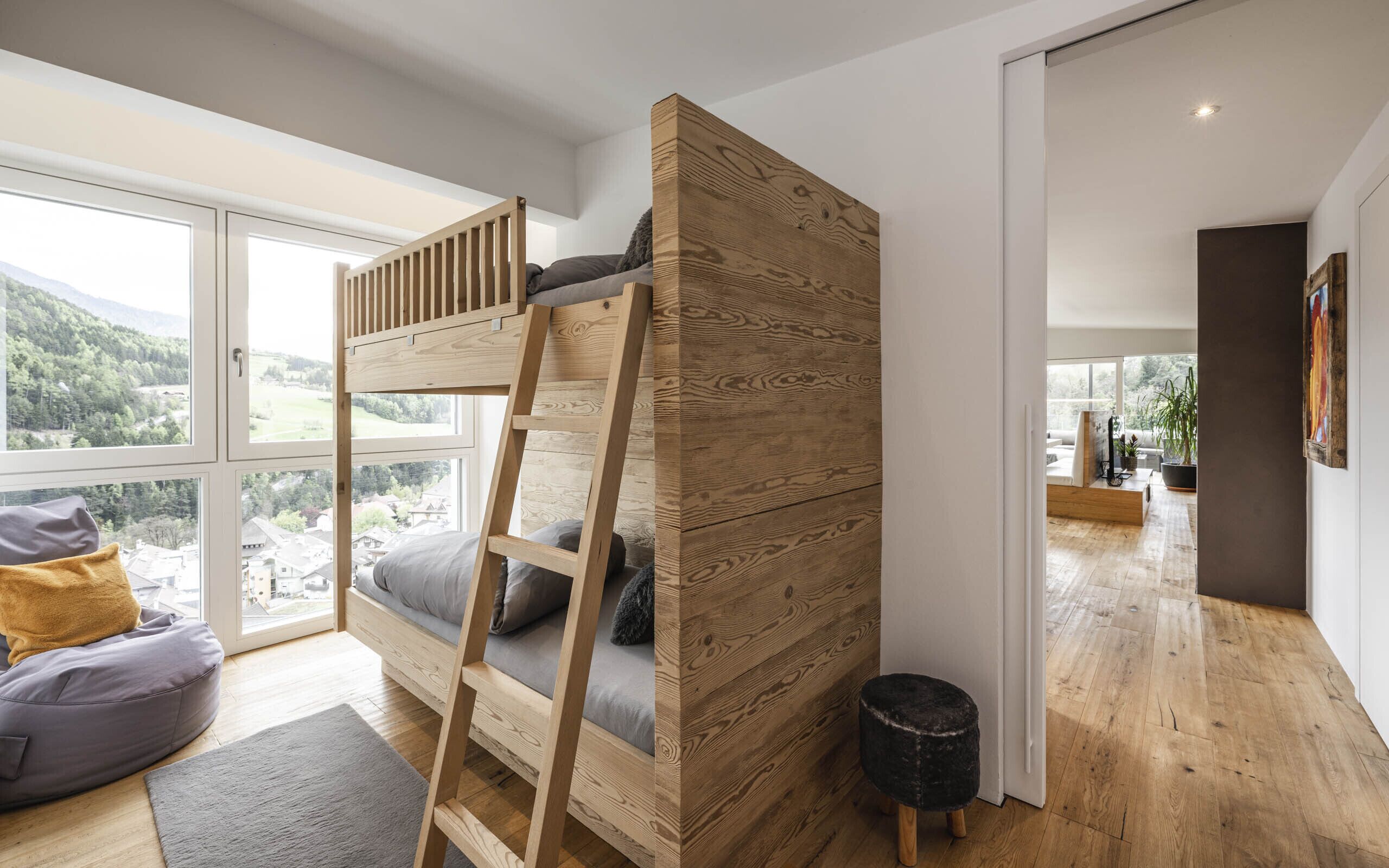 Une chambre moderne avec un lit superposé, de grandes fenêtres et une vue sur un paysage montagneux.