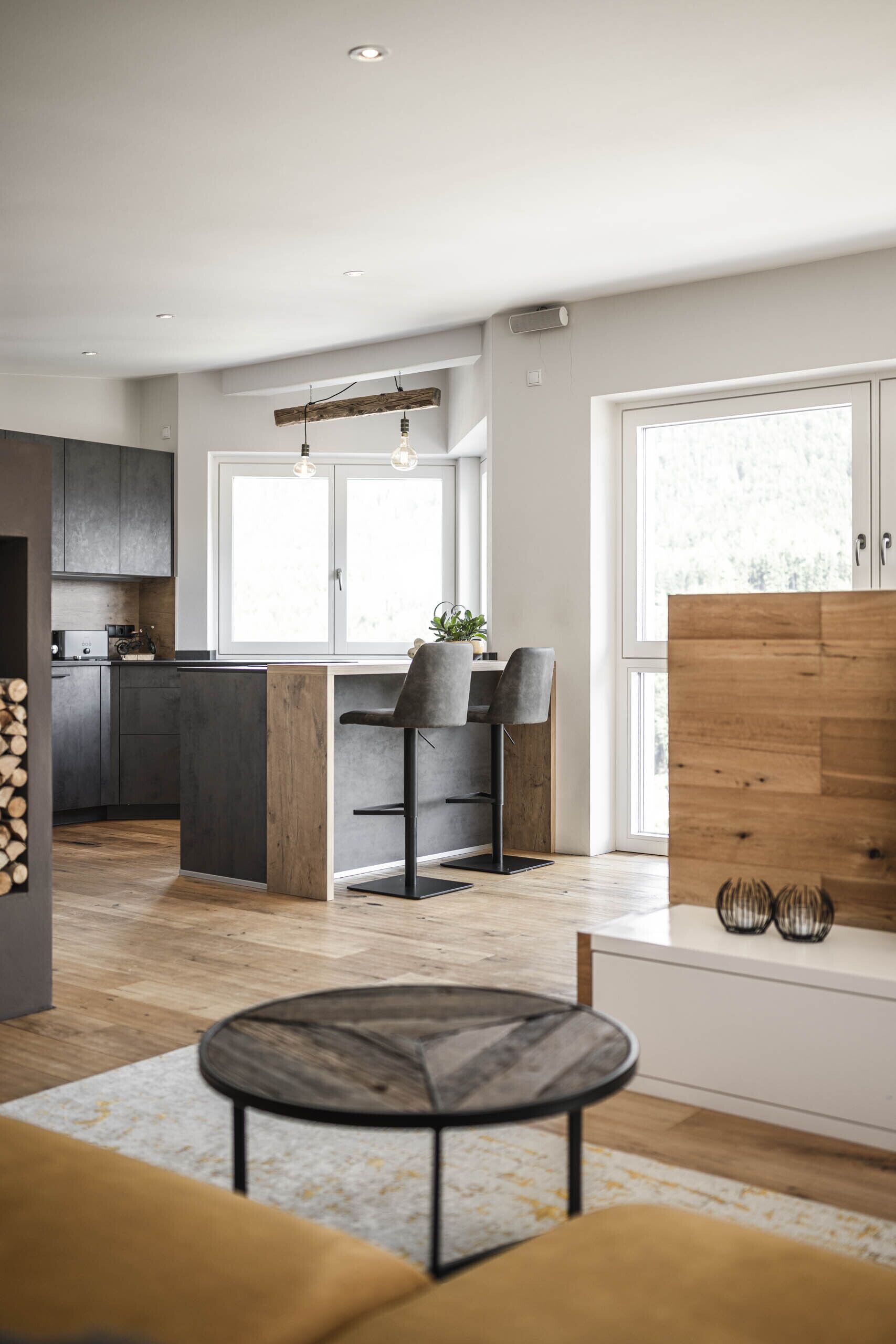 Eine moderne Küche mit dunklen Schränken, einer Holztischinsel und einem Essbereich mit zwei Stühlen.