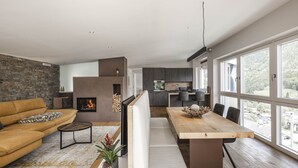 A modern living room with a stone wall, a fireplace, a wooden dining table, and a view of the kitchen and outdoors. - Dolomites Alpin Penthouse 90 qm with privat sauna and privat whirlpool, WLAN (Rio di Pusteria)