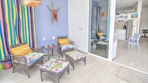 Una habitación con muebles de mimbre, una cortina a rayas y un vidrio que da a una zona de cocina.