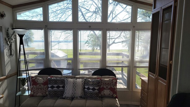 A cozy room with a large bay window, a sofa with patterned cushions, a small table, and a floor lamp.