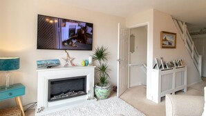 A living room with a fireplace, a television mounted above it, and a staircase leading to another level. - Cosy Seaside Home with Free Parking - Pass the Keys (North Shields)