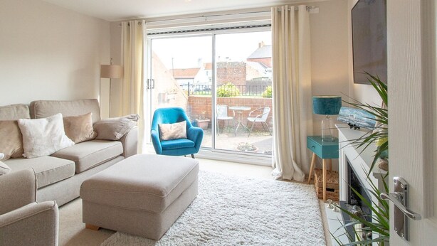 A modern living room with a sofa, ottoman, and a blue armchair. - Cosy Seaside Home with Free Parking - Pass the Keys (North Shields)