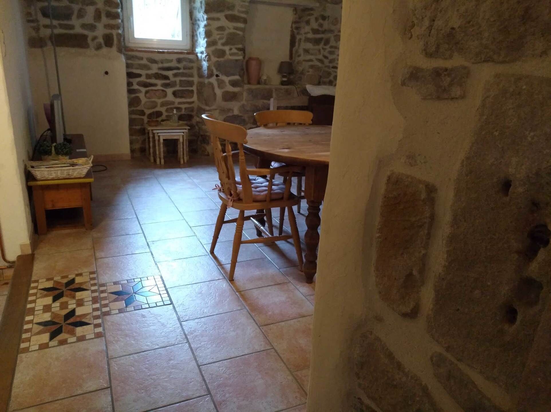 A stone-walled room with a tiled floor, a wooden dining table with chairs, and a small table with a basket.