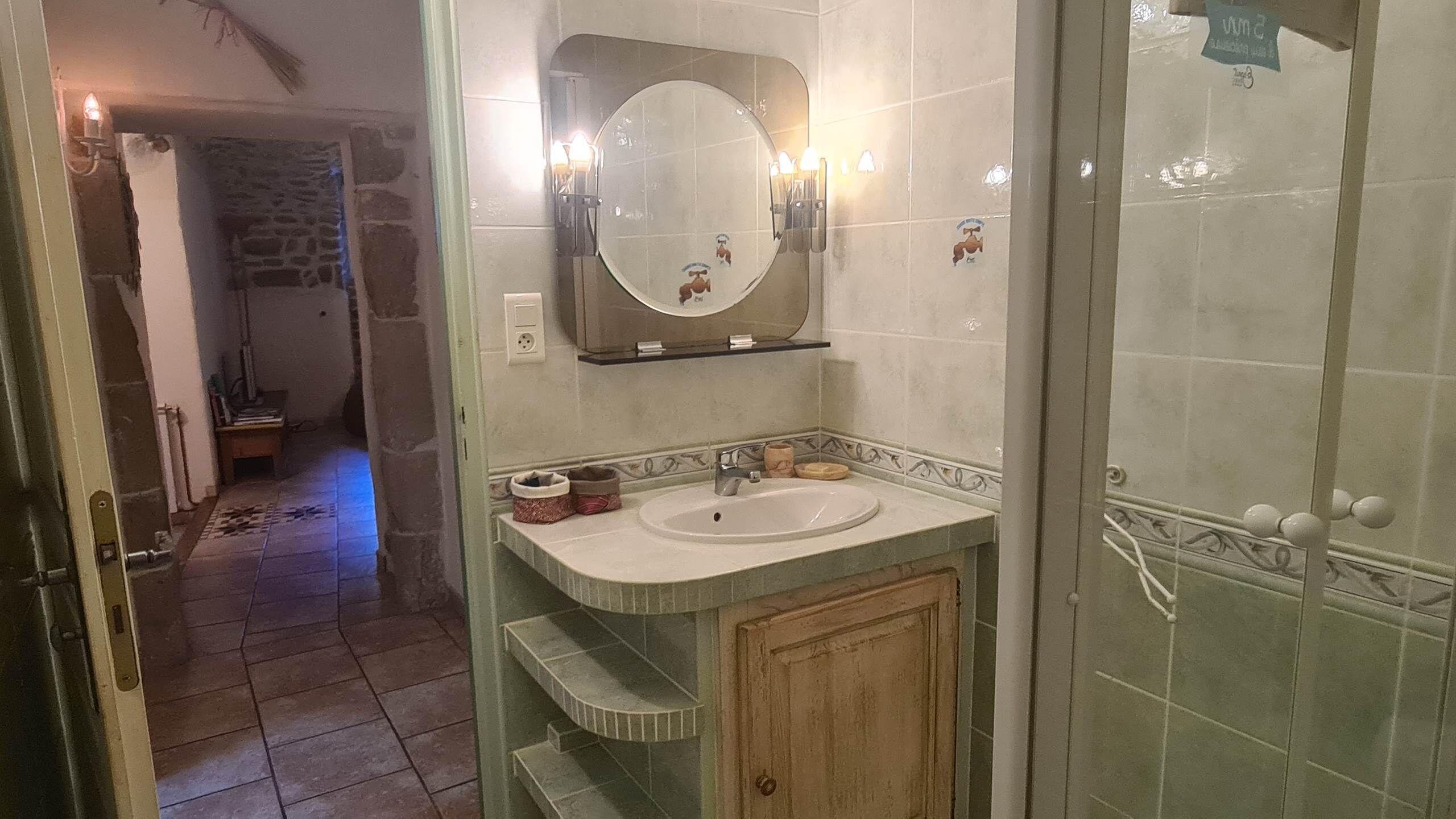 Un baño con lavamanos, espejo y perchero. Hay una puerta de madera y una pared con azulejos.