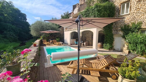 A pool area with lounge chairs and umbrellas, surrounded by stone buildings and greenery. - The southern sun - 4 people (ST JEAN DE VALERISCLE)