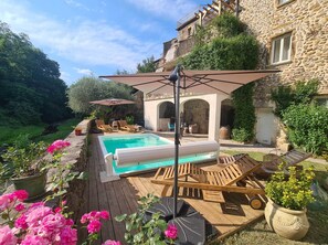 A pool area with lounge chairs and umbrellas, surrounded by stone buildings and greenery. - The southern sun - 4 people (ST JEAN DE VALERISCLE)