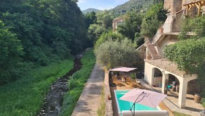 A riverside property with a pool, outdoor seating, and a stone building with a balcony. - The southern sun - 4 people (ST JEAN DE VALERISCLE)