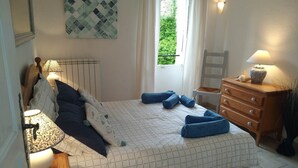 Quarto com cama, cómoda, mesa de cabeceira, janela com cortinas e luminária na parede.
