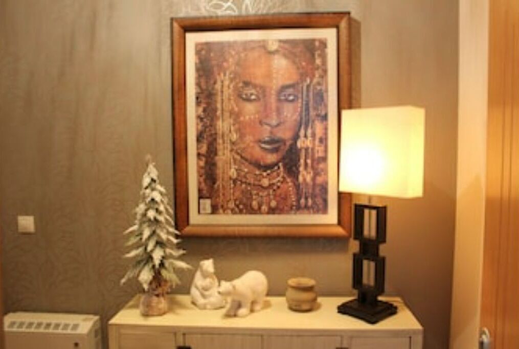 A framed artwork on the wall, a small potted plant, a white cat figurine, a lamp, and a small table with a vase.