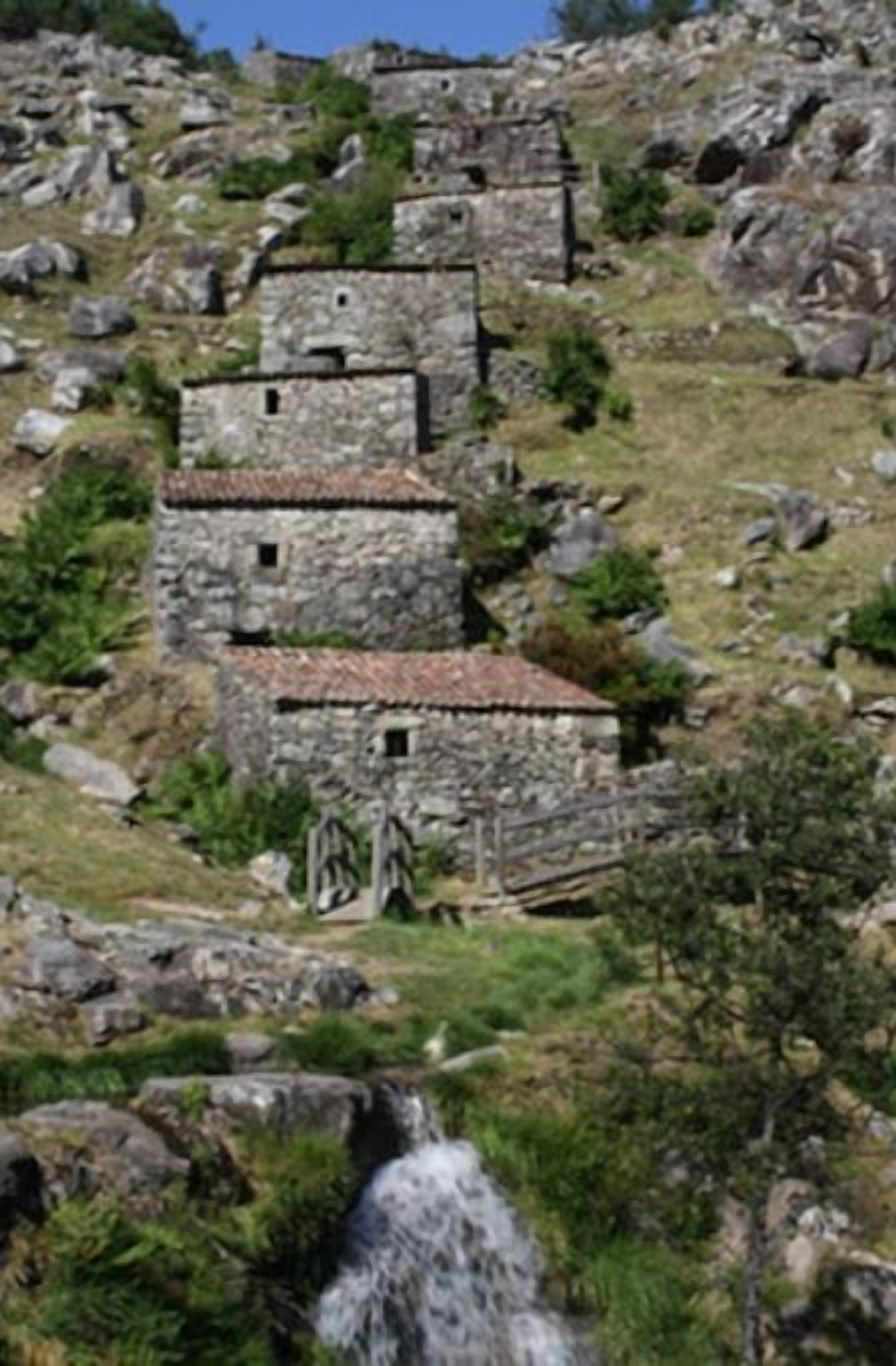 A stone building with multiple levels, situated on a rocky hillside.