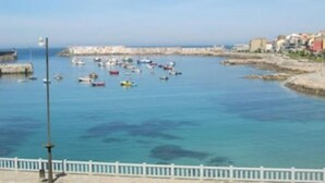 A coastal marina with boats, a white fence, and buildings in the background.