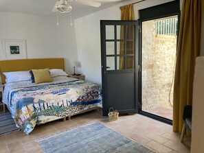 A bedroom with a bed, a nightstand, a lamp, a ceiling fan, a door leading to a balcony, and a window with curtains.