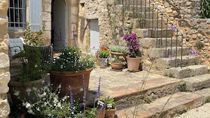 Un edificio de piedra con una escalera que lleva a una puerta. Hay plantas y flores en macetas frente al edificio.