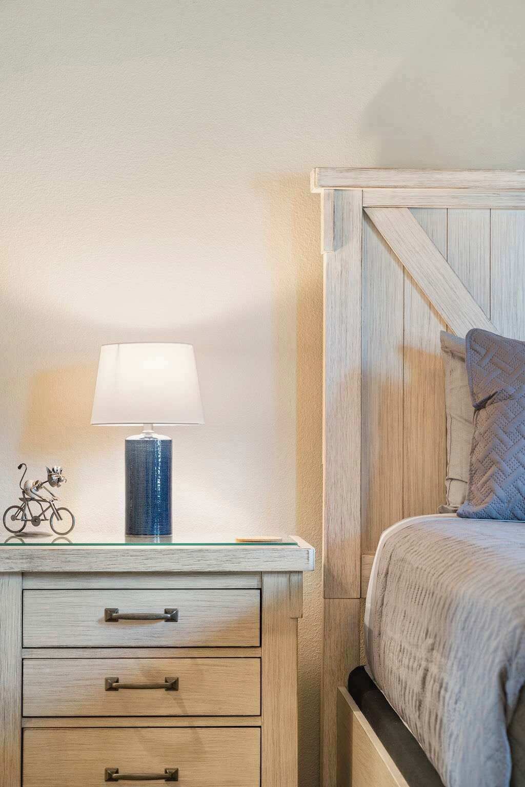 Een slaapkamer met een houten hoofdbord, een nachtkastje met een lamp en een klein decoratief object.