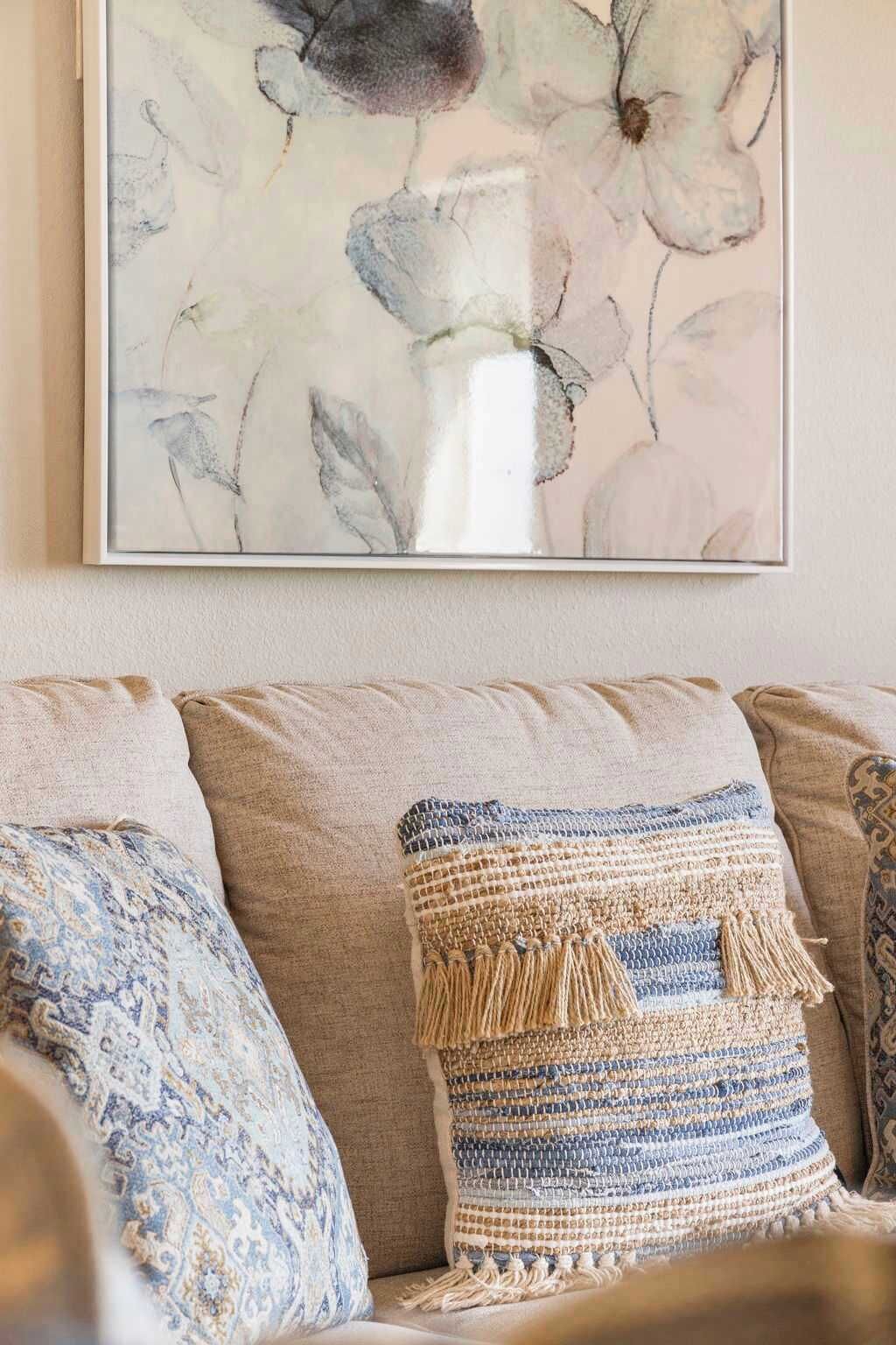 A living room with a beige sofa, patterned cushions, and a framed floral artwork on the wall.