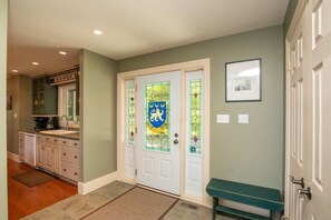 Un couloir avec une porte à deux battants, un banc et un coin cuisine équipé de placards et d’un plan de travail.