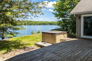 Une terrasse dotée d’un jacuzzi, offrant une vue sur un lac bordé d’arbres et un ciel dégagé.