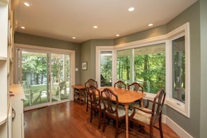 A dining area with a wooden table and chairs, large windows with a view of greenery, and a ceiling with recessed lighting. - Panorama Cottage - perfect sunsets! (Parry Sound)