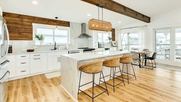 Una cocina moderna con armarios blancos, una isla grande con taburetes de bar, una lámpara colgante y vistas de la ciudad a través de amplios ventanales.