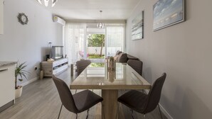 Ein moderner Essbereich mit einem Glastisch, vier Stühlen, einer Couch und Blick ins Freie.