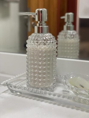 Un tocador de baño con un dispensador de jabón transparente y texturizado, y un jabonera.