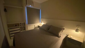 A bedroom with a bed, bedside tables, a wardrobe, and a nightstand with a lamp. - AMETISTA (Maceió)