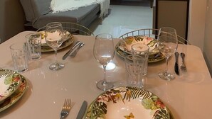 A dining area with a table set for four, a sofa in the background, and a decorative ceiling light fixture. - AMETISTA (Maceió)