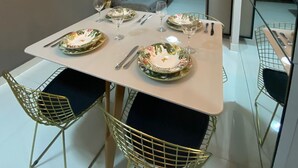 A modern dining area with a white table set for four, surrounded by gold wire chairs. - AMETISTA (Maceió)