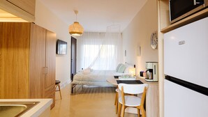 Ein modernes Hotelzimmer mit Küchenzeile, einem Himmelbett, einer Essecke mit Tisch und Stühlen sowie einem großen Spiegel.