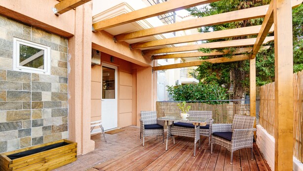 Eine überdachte Terrasse mit Korbmöbeln, einer Steinwand und einer Holzpergola.
