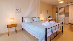 Ein Schlafzimmer mit einem Bett, Nachttischen, einer Stehlampe, einer Wanduhr und einer Küchenzeile mit Schränken und einem Herd.