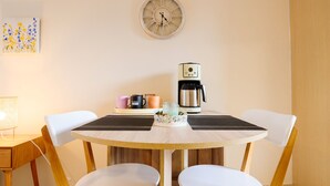 Ein runder Holztisch mit zwei weißen Stühlen, einer Kaffeemaschine und einer Uhr an der Wand.