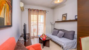 Una sala de estar con un sofá, una televisión, una mesa con un objeto decorativo y una ventana con cortinas.